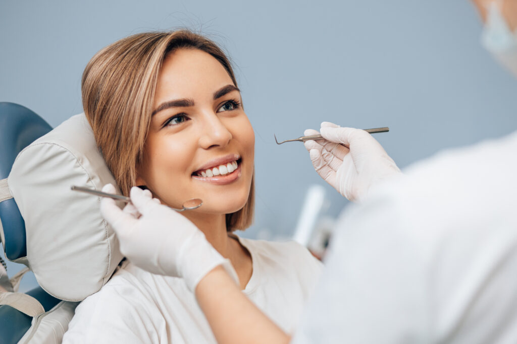 attractive woman with short hair sit in dental office and look at doctor with confidence, she has perfect smile. professional doctor of clinic use special sterilized medical instruments